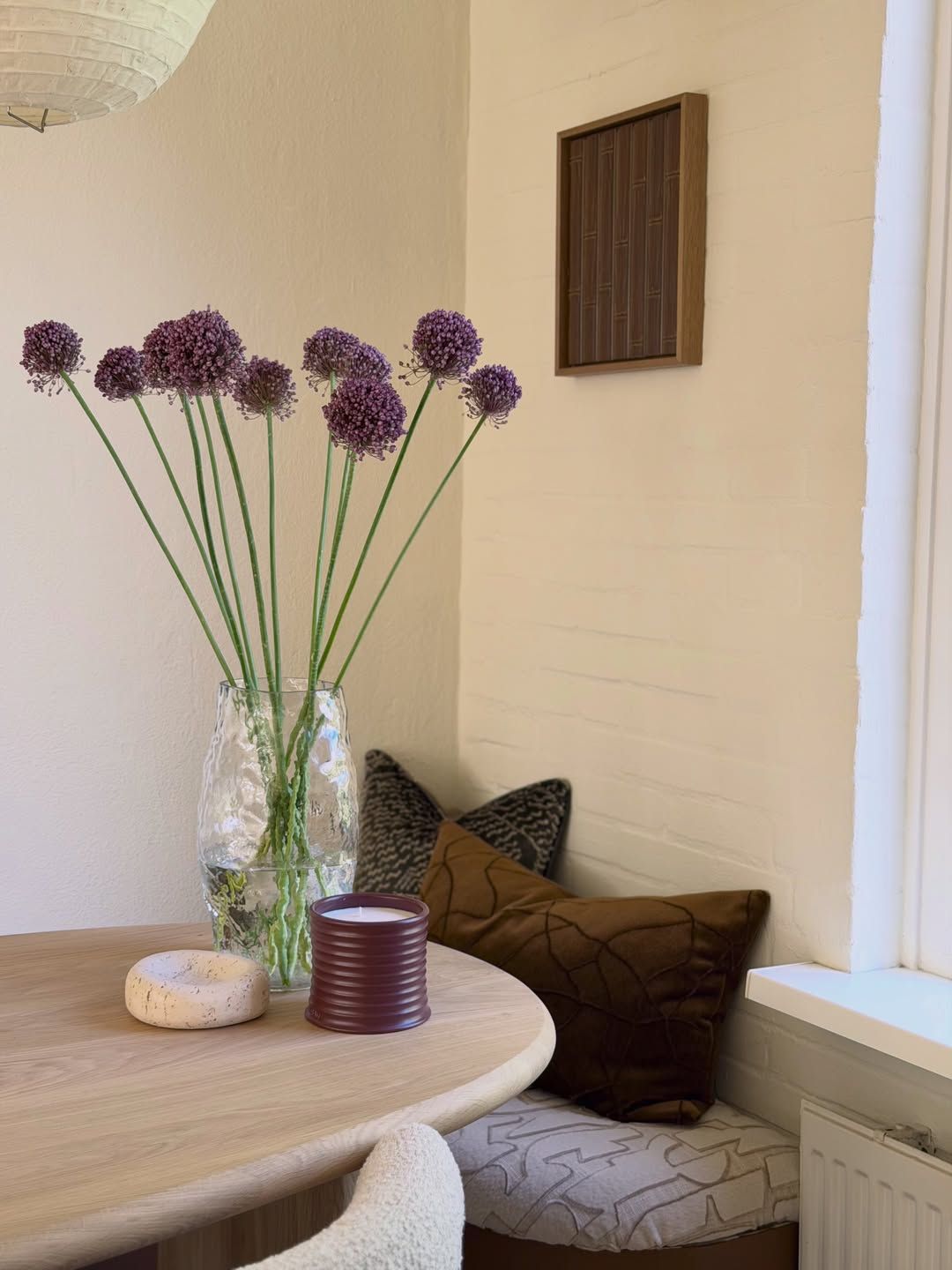Round dining table with purple alliums in a glass vase and a bench with cushions