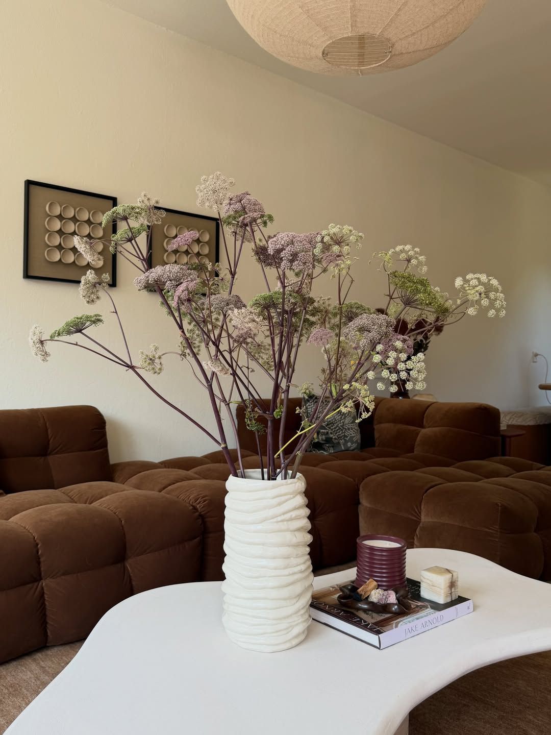 Living room with a brown modular sofa, white vase with flowering branches and framed art