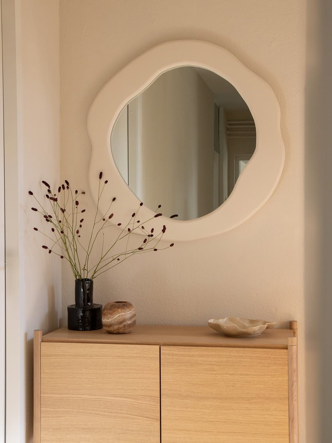 Wavy white mirror above an oak sideboard with dried branches